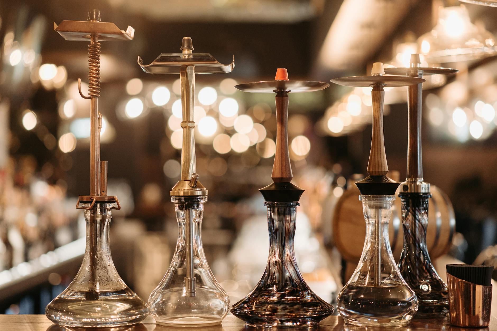 A row of elegant hookahs displayed on a bar counter with warm bokeh lighting